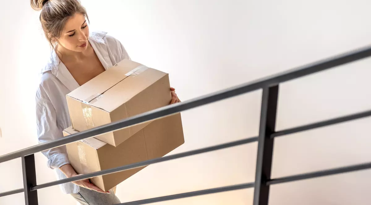 retururisimple.ro: femeie blonda, par prins intr-un coc urca scarile cu o cutie in brate