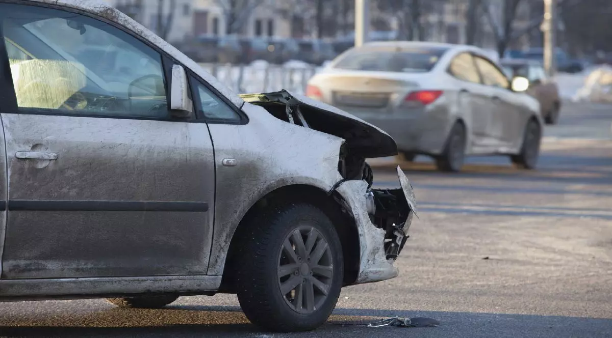 Fotografie cu un sedan alb cu partea frontală grav avariată, parcat pe o stradă înzăpezită, cu un sedan alb în fundal.
