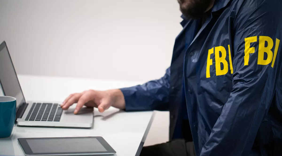 Un agent FBI în timp ce lucrează la un laptop. Poartă jacheta pe care scrie cu galben FBI
