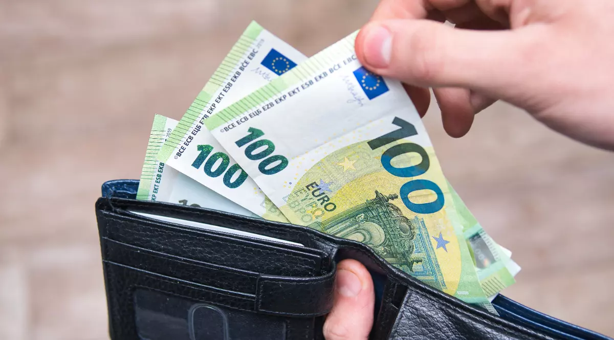 Un bărbat care scoate dintr-un portofel negru trei hârtii de câte 100 de euro