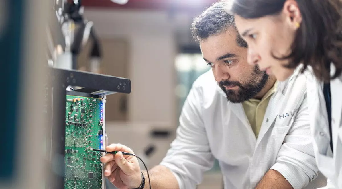 Un bărbat și o femeie, îmbrăcați în halate albe, lucrează la o placă de bază a unui computer