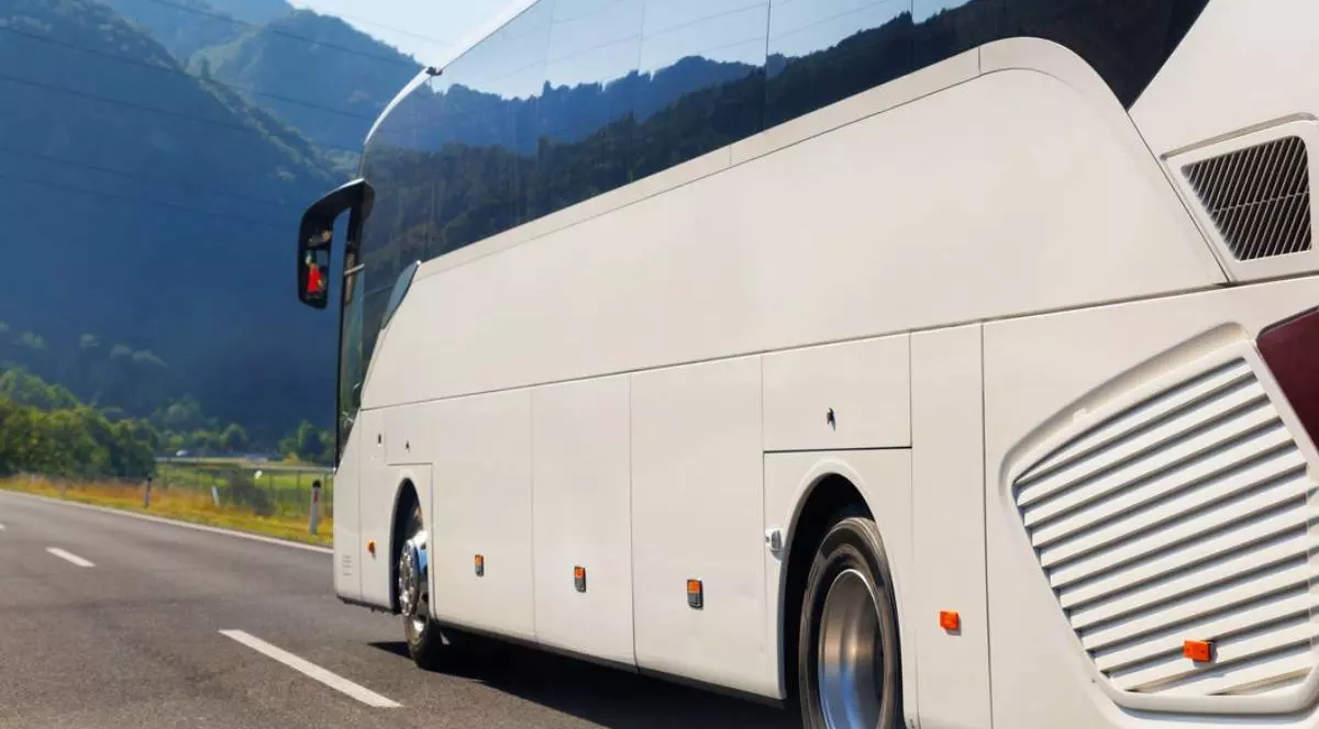 Vedere din spate pitorească, autobuz turistic alb, mare, luxos, confortabil, care circulă pe autostradă, într-o zi însorită, peisaj montan, fundal. Călătorii și autocar