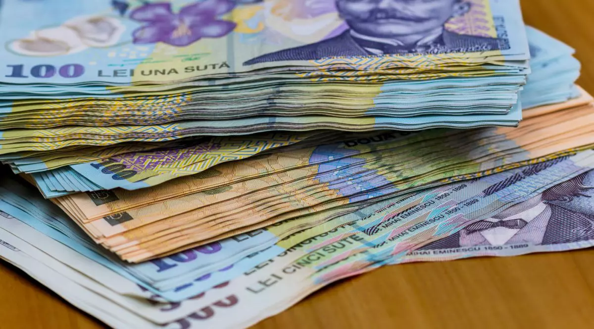 Bani pe o masă de lemn, bancnote de 100 de lei, 200 de lei și 500 de lei, în teancuri, pe o masă de lemn