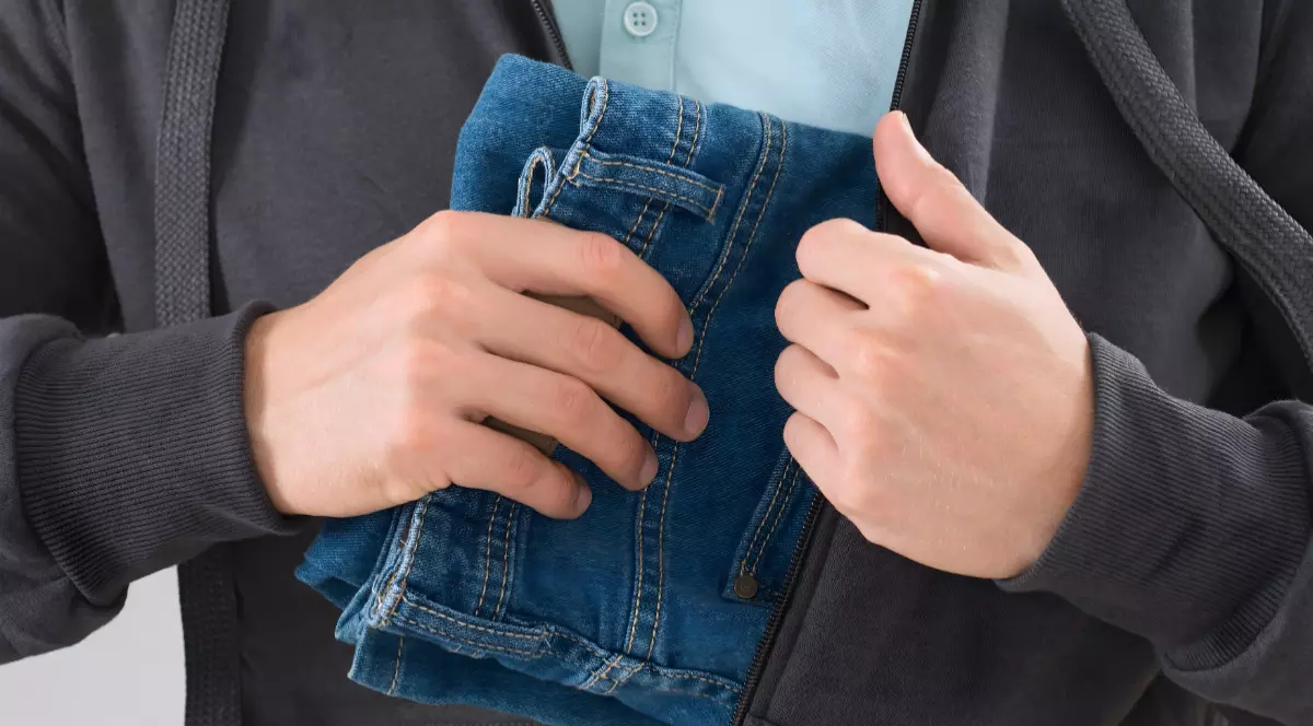 Un bărbat care ascunde în hanorac o pereche de blugi.