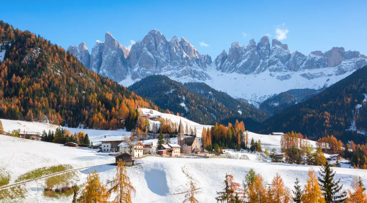 Biserica Sfânta Magdalena din Dolomiți, așezată într-o vale, sub crestele muntoase acoperite de zăpadă.