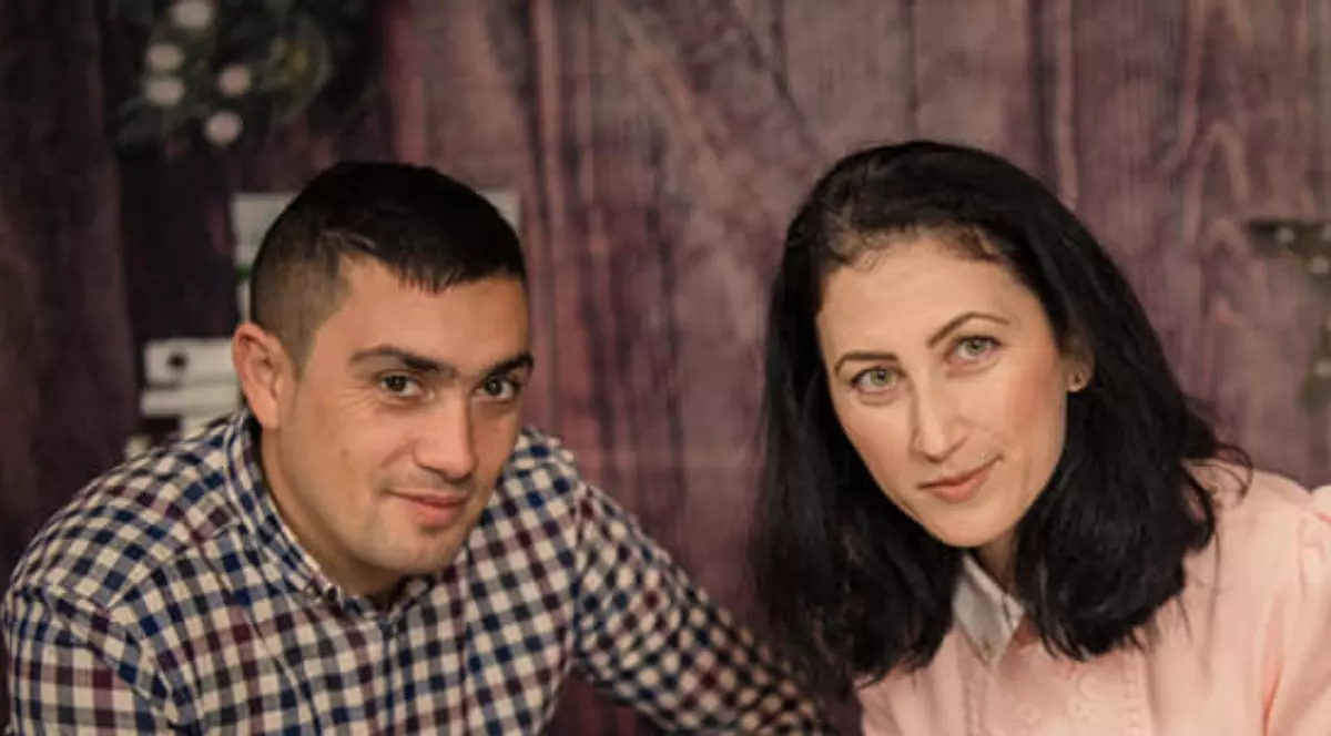 În imagine apar un bărbat și o femeie așezați unul lângă celălalt, privind direct către cameră.