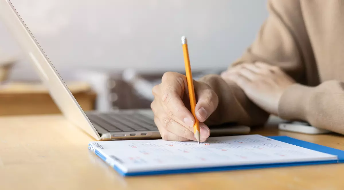 Un bărbat care stă la birou și bifează cu un creion un calendar.