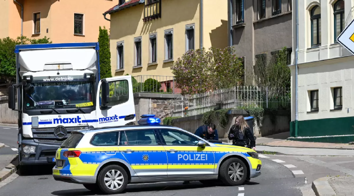 O mașină de poliție oprită în fața unui camion, într-un oraș din Germania. polițiștii completează niște acte pe capota mașinii.