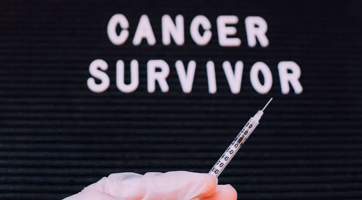 Pe un ecran negru scrie cu alb Cancer Survivor si o mana imbracata cu o manusa de protectie are o seringa cu ac indreptata spre scris. Cancere care se pot trata. Medici despre preventie si depistare. Foto Envato