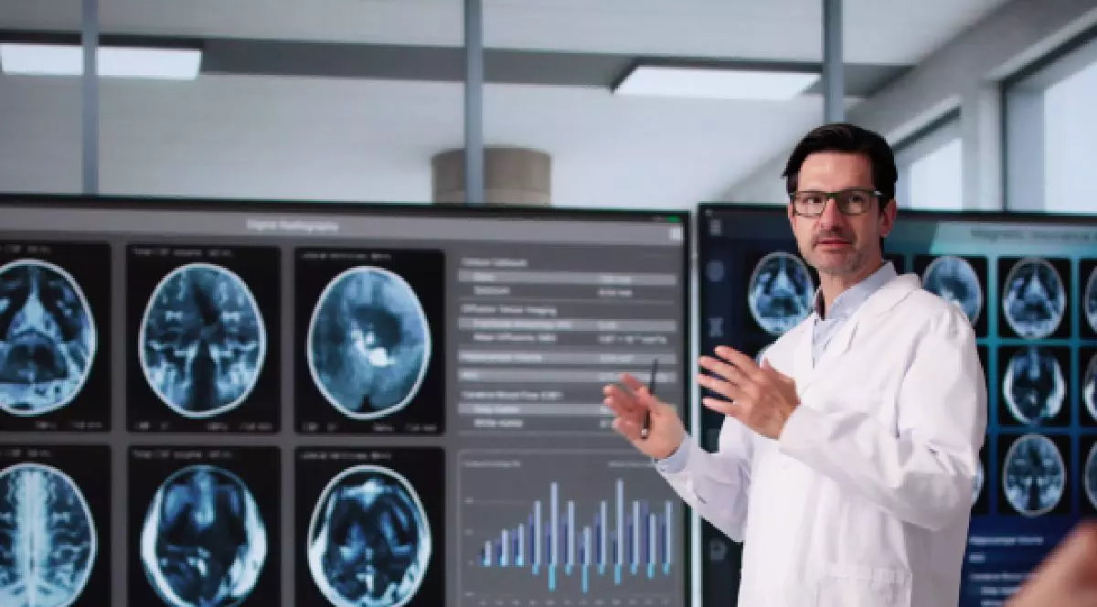 Un medic imbracat in halat alb sta in picioare si vorbeste cu un alt coleg care sta jos si se uita la imagini radiografice. Centre de expertiza in boli rare. Foto Imago