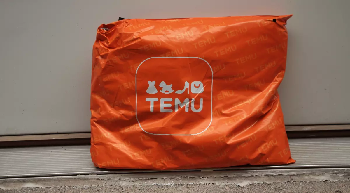 Imaginea arată un colet portocaliu inscripționat cu logo-ul Temu, lăsat în fața unei uși, sugerând o livrare.