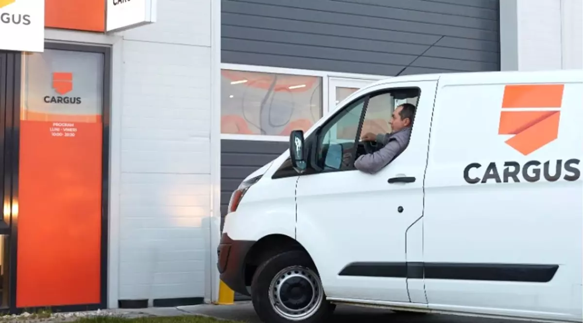O dubă de curierat albă de la Cargus cu un curier la volan, în timp ce parchează în fața sediului