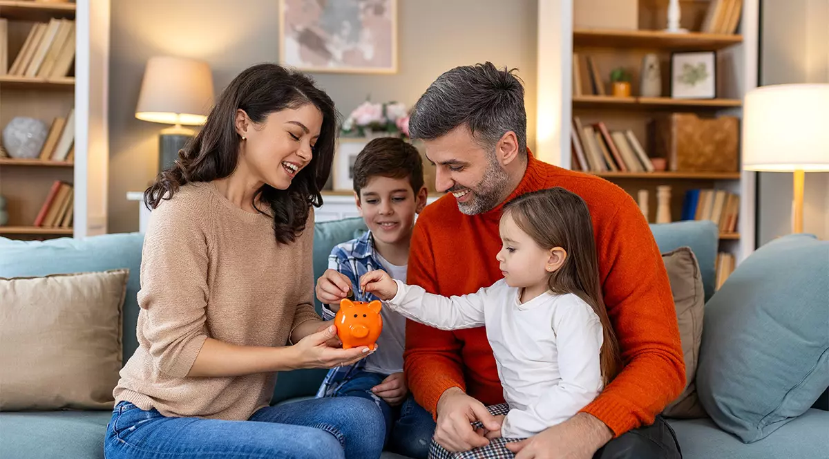 O familie formată din părinți și copii pun bani la pușculită în ideea că cheltuirea banilor și investirea lor trebuie realizată cu cap.