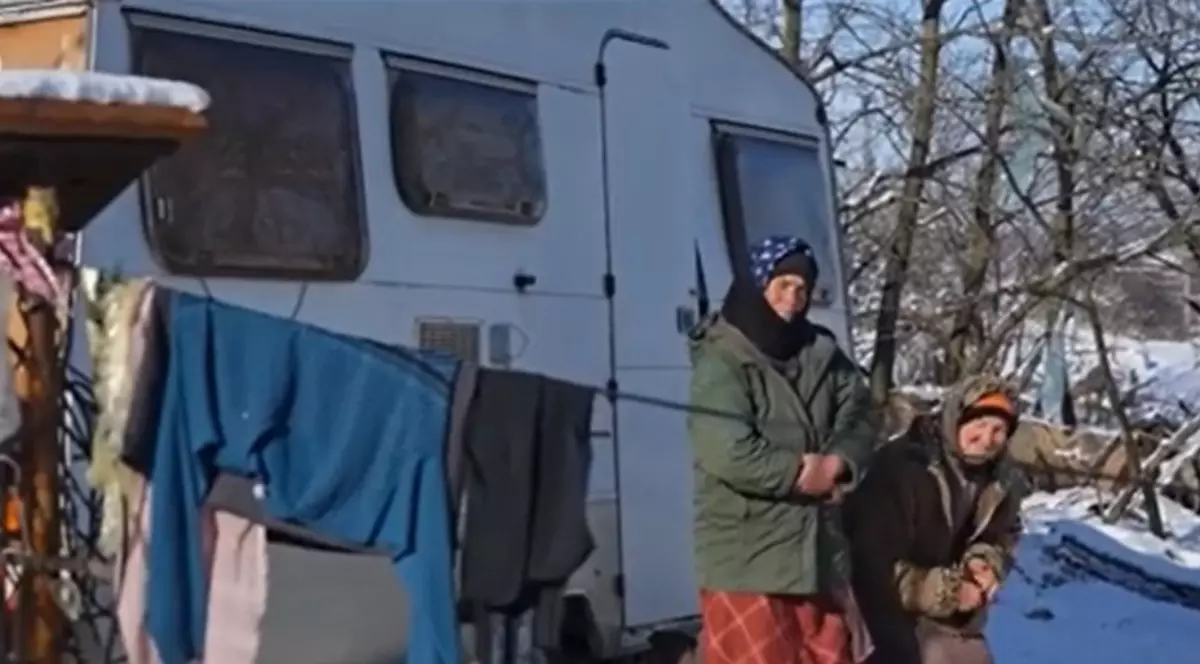 Două femei îmbrăcate gros, cu batic în cap stau lângă o rulotă, afară e frig și este zăpadă