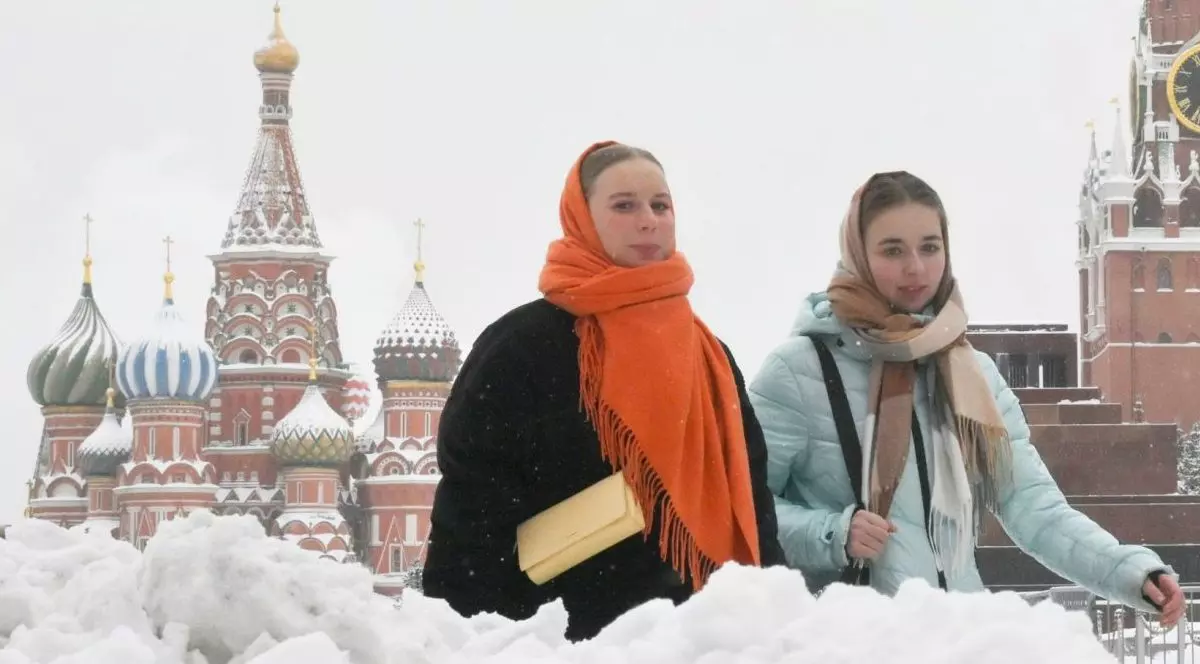 Fete se plimbă în Piața Roșie, cu Turnul Spasskaya din Kremlin și Catedrala Sfântul Vasile în fundal, în timpul unei ninsori abundente la Moscova, Rusia.