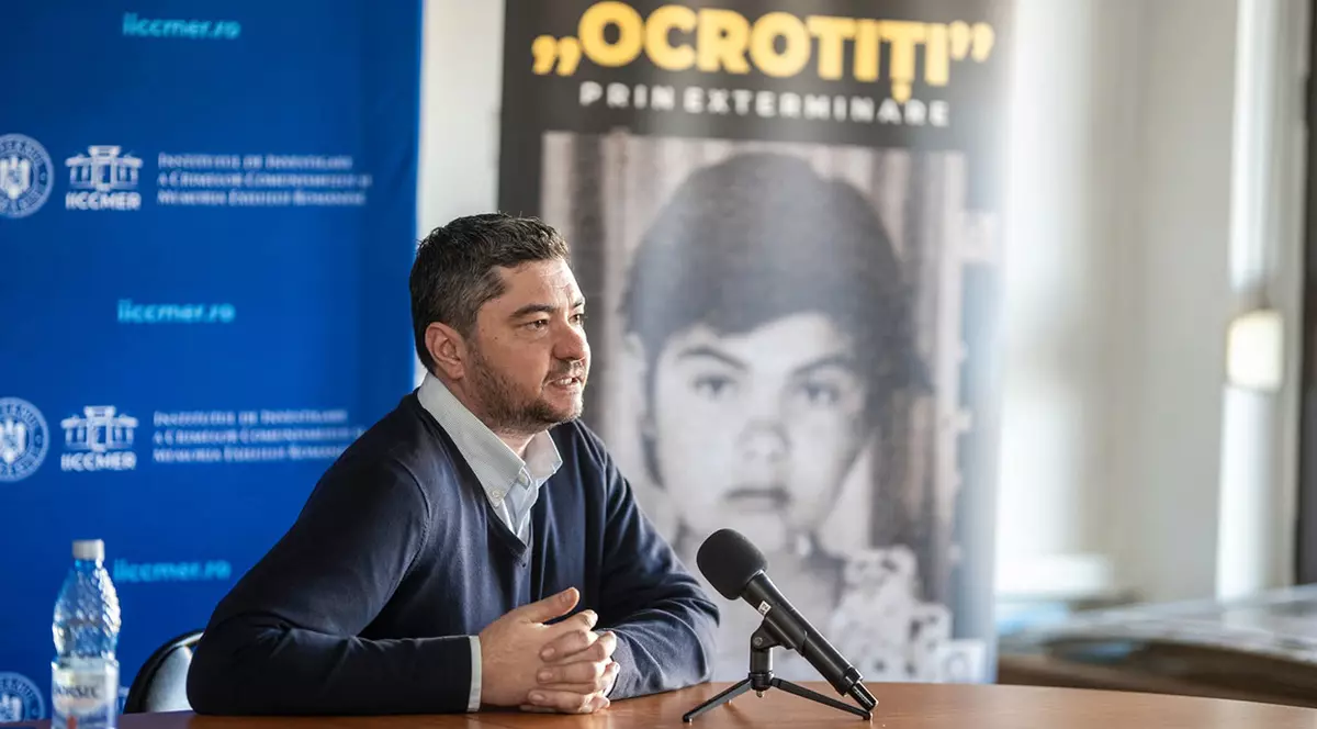 Dr. Florin Soare, istoricul care a semnalat ororile petrecute în căminul pentru copii irecuperabili de la Moreni-Țuicani. Imbracat in pulovar bleumarin si camasa alba, sta la un boriu si vorbeste la un microfon. In spate se vede un poster cu un copil