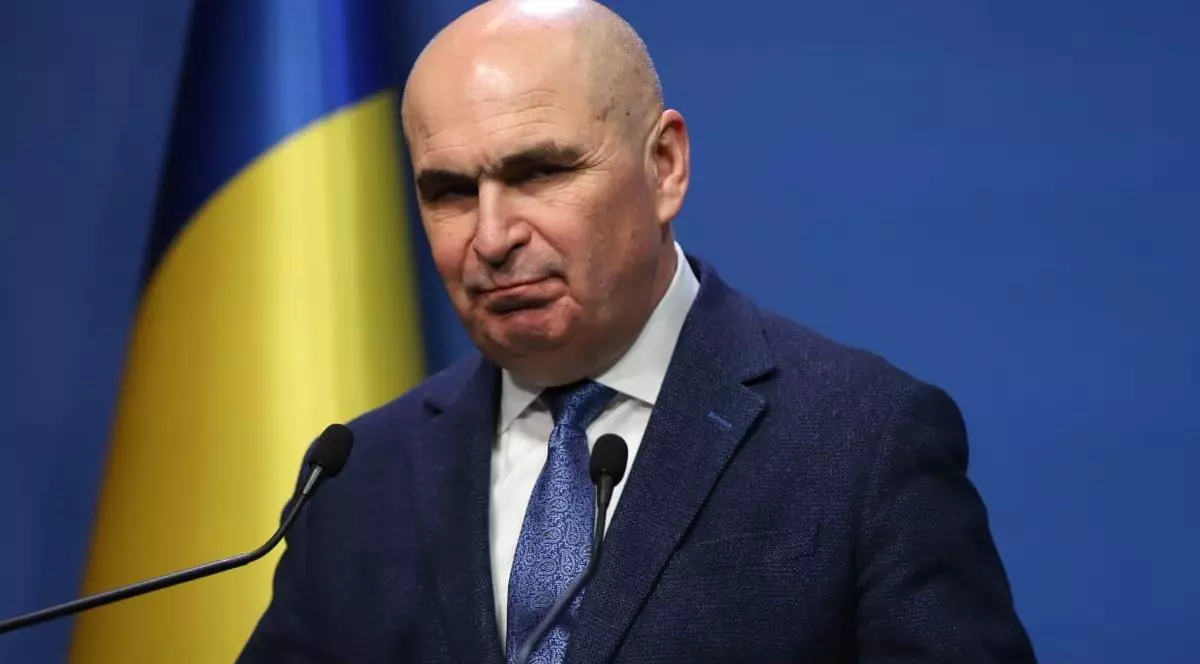 Ilie Bolojan in conferinta de presa, gesticuleaza larg cu mainile. Ilie Bolojan poarta un costum albastru deschis, o camasa alba si cravata albastru deschis. In spate se vede un drapel tricolor