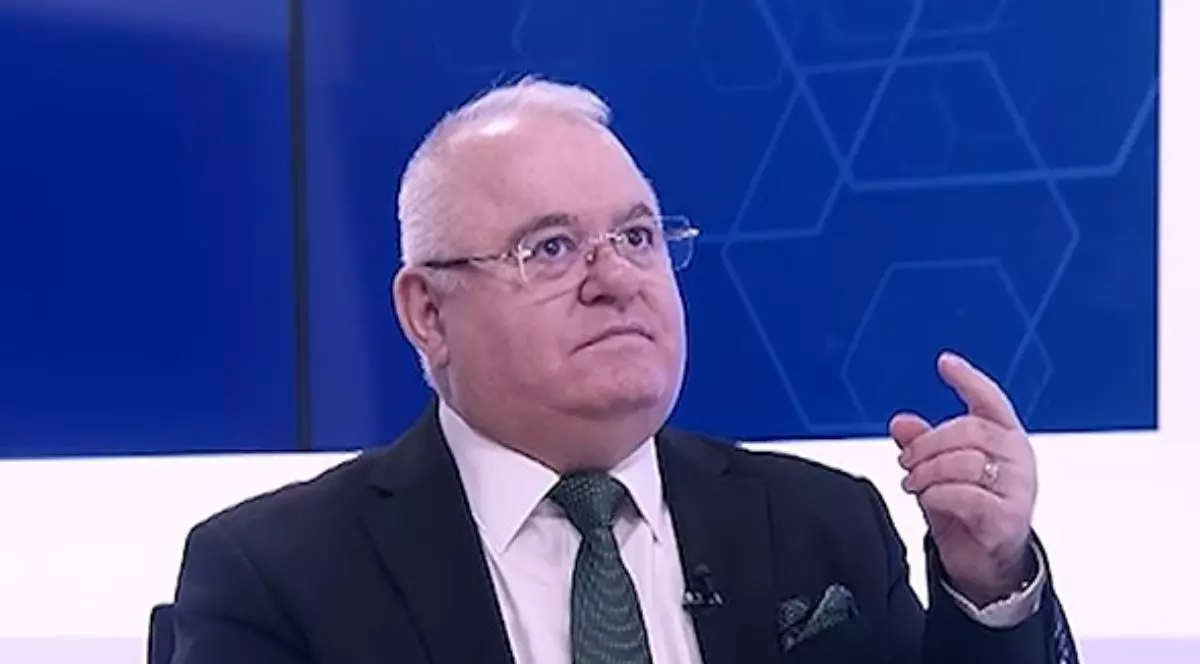 Ion Duvac, îmbrăcat într-un sacou negru, cu o cămașă albă și o cravată gri, stând cu mâna ridicată, cu un deget în sus