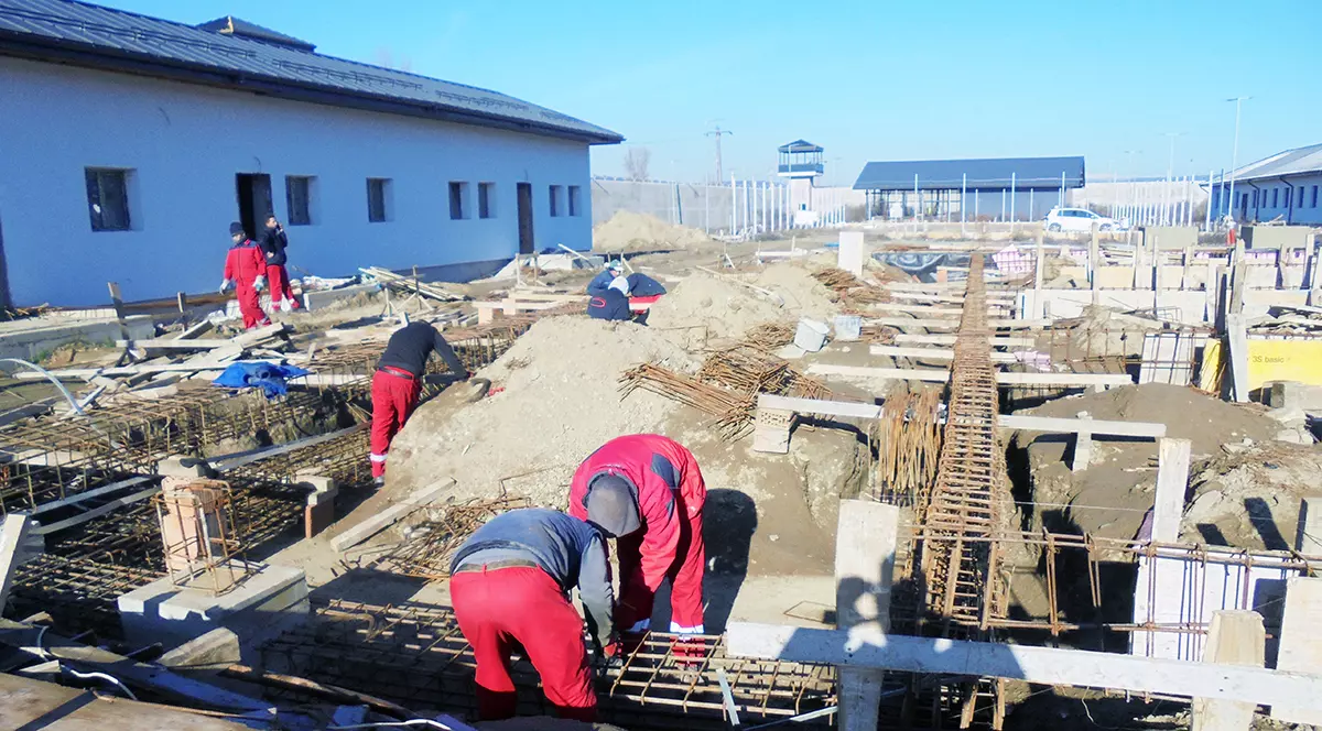 Mai multi muncitori imbracati in salopete rosii lucreaza pe un santier