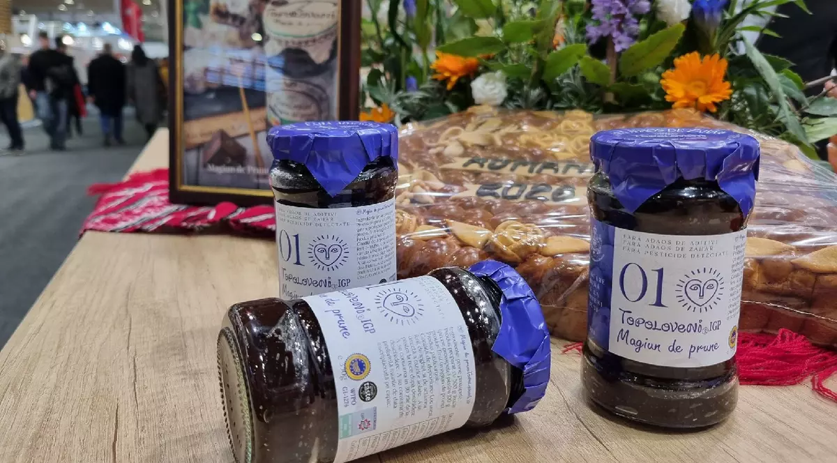 Trei borcane de magiun de prune Topoloveni pe o masă, la o expozitie, în fundal se vede o pâine si o rama foto