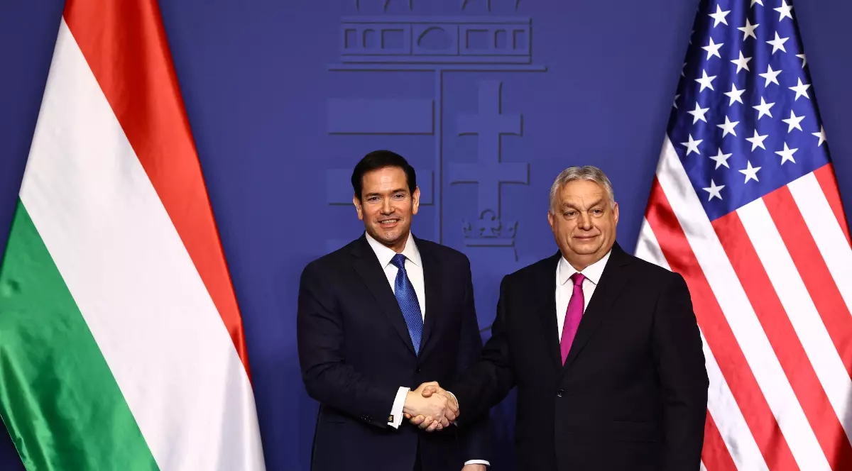 Marco Rubio și Viktor Orbán își strâng mâna în cadrul unei întâlniri oficiale, având în spate steagurile Ungariei și Statelor Unite. Cei doi apar îmbrăcați formal, într-un cadru diplomatic pregătit pentru declarații sau negocieri.