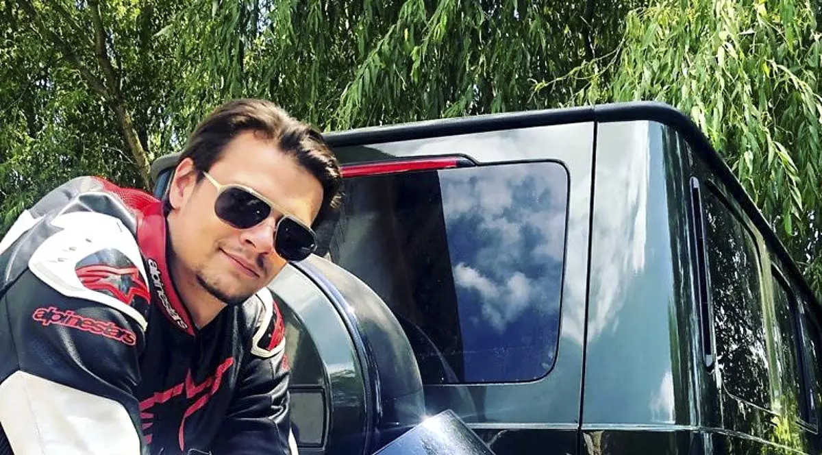 Un tanar cu ochelari de soare la ochi langa o motocicleta