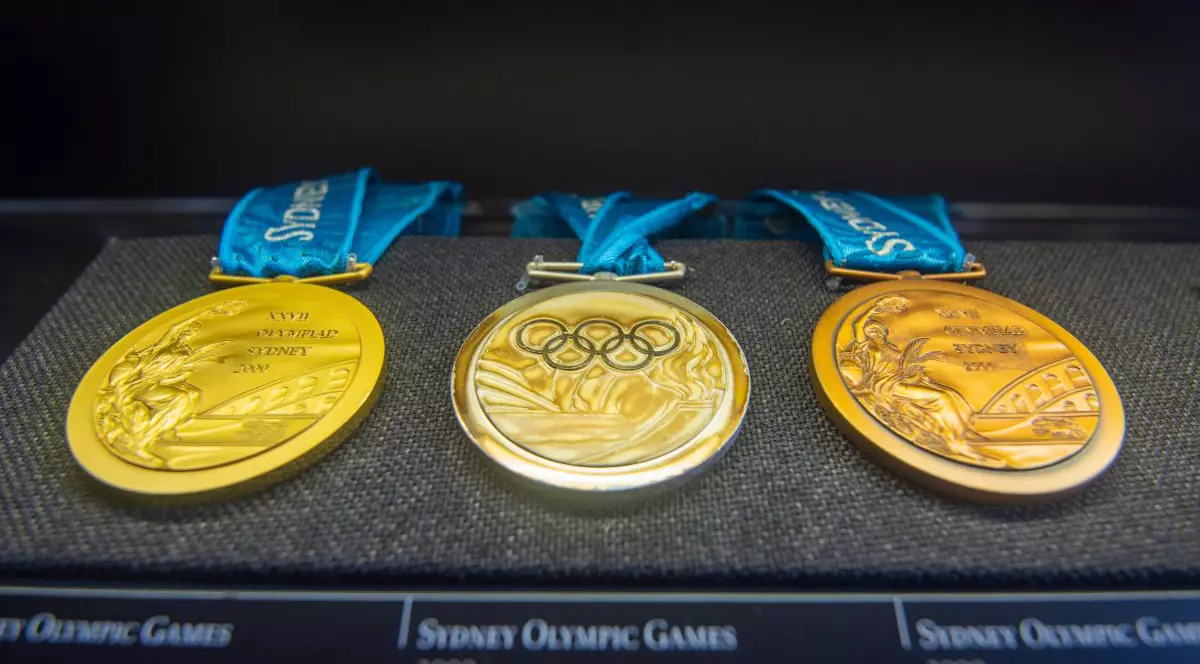 Trei medalii de la Jocurile Olimpice, fiecare cu șnur de culoare albastră, puse pe o tavă de burete de culoare neagră