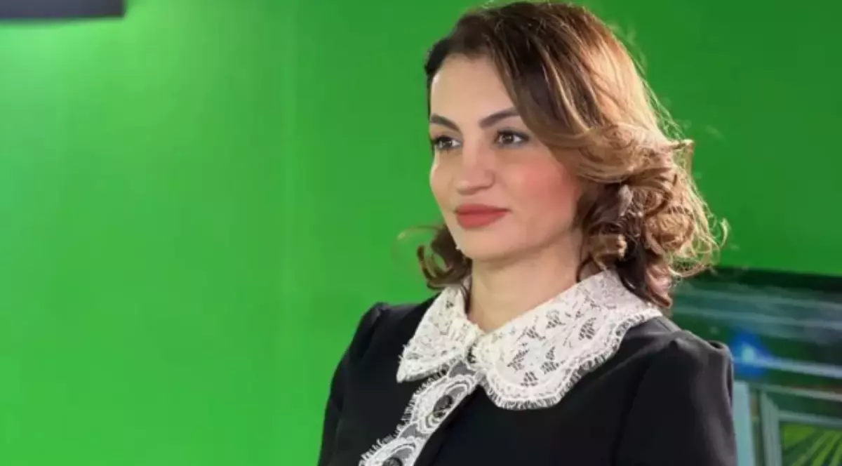 Mihaela Neagu într-o rochie neagră, în timp ce face o poză. În fundal se observă un panou verde.