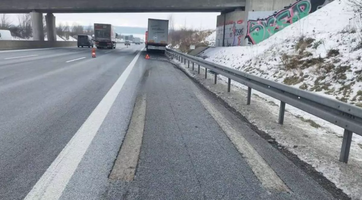 Suprafață de drum deteriorată pe acostament , se vad in fata doua camioane, sub un pod, pe marginea drumului se vede zapada