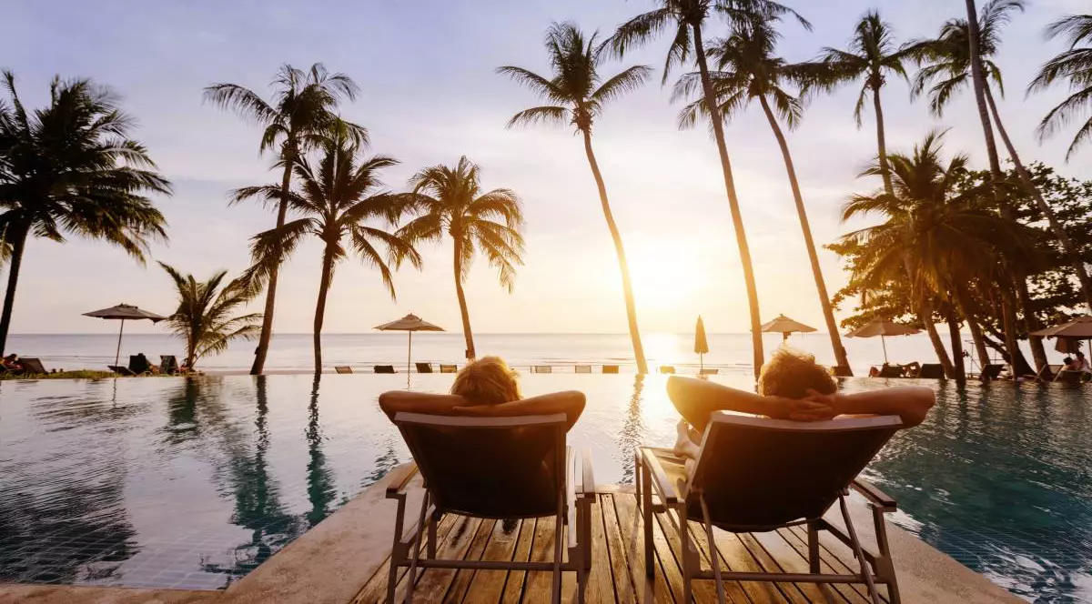 Cuplu în luna de miere, în vacanță la un hotel de lux pe plajă, bărbat și femeie relaxându-se lângă piscină la apus, se vad palmieri