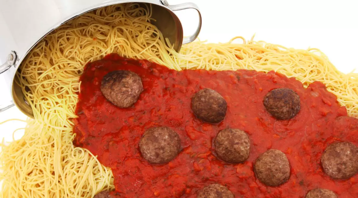 Oală mare de tăiței de spaghete cu chiftele și sos vărsat pe fundal alb