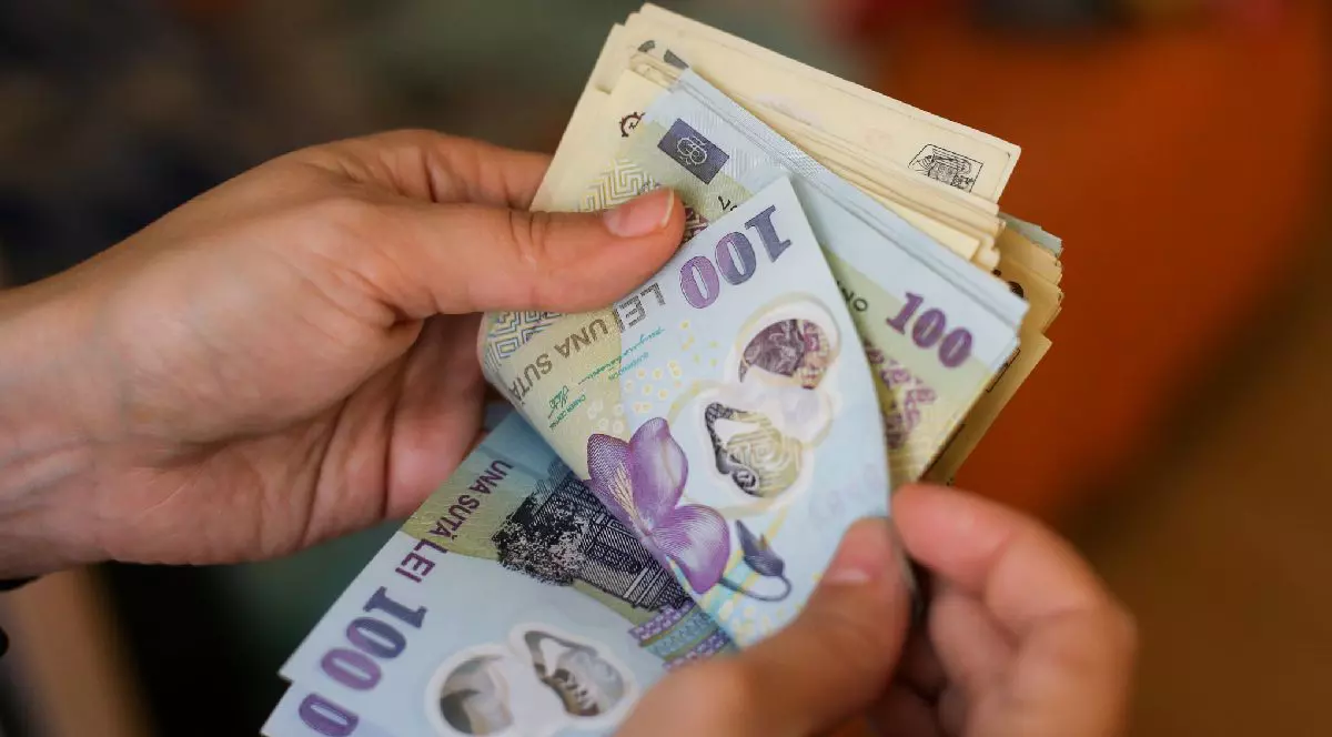 Prim-plan cu mâinile unei persoane care ține un teanc de bancnote românești.