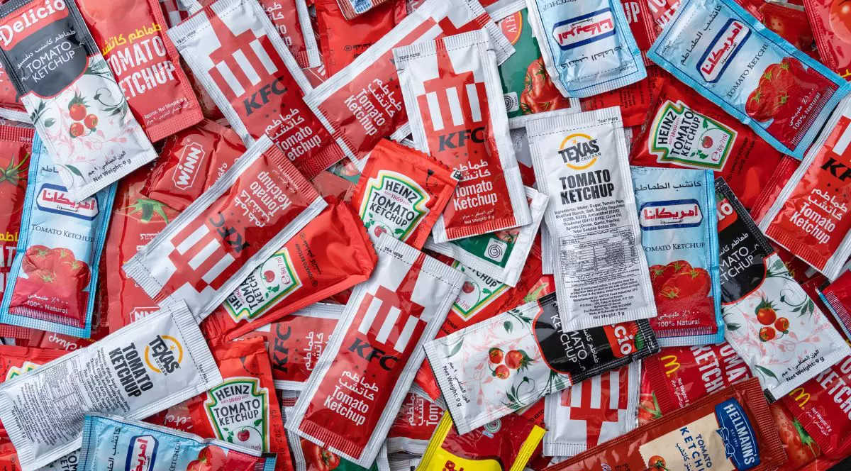 O mulțime de pliculețe de ketchup, unul peste altul, de culoare roșie, albă și albastră