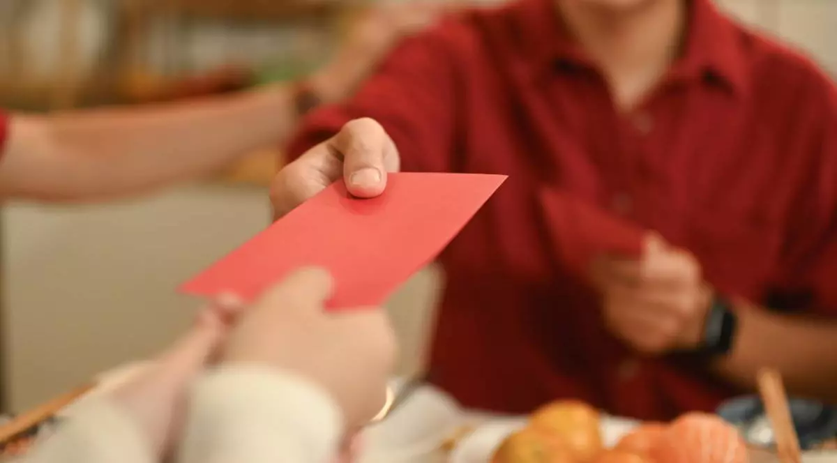 Prim-plan cu o mână care oferă un plic roșu sau un Hongbao în timpul sărbătorii festive a Anului Nou Chinezesc