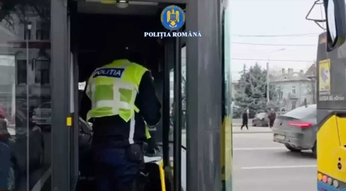 În imagine se vede un polițist care urcă într-un mijloc de transport public, aparent un autobuz sau troleibuz, pentru a efectua un control.