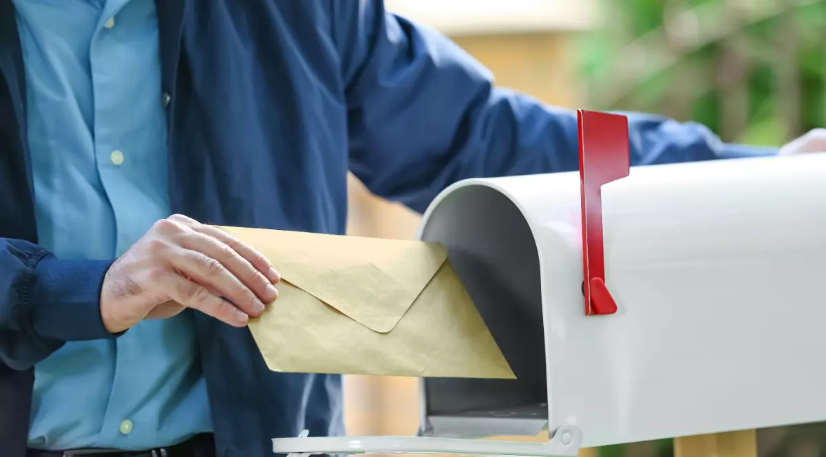 Un poștaș care pune un plic într-o cutie poștală.