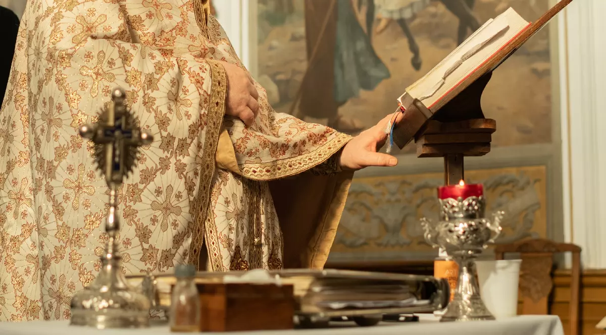 Un preot în sutană se roagă și citește Biblia