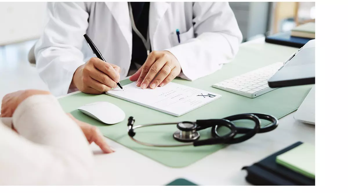 Un medic imbracat in halat alb sta la birou si scrie. Prima zi de concediu medical e și neplătită, și tăiată din vechimea la pensie. Foto Shutterstock