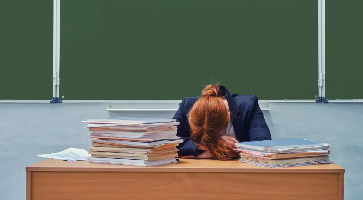 Profesoară care stă cu capul sprijinit pe brate, pe catedra