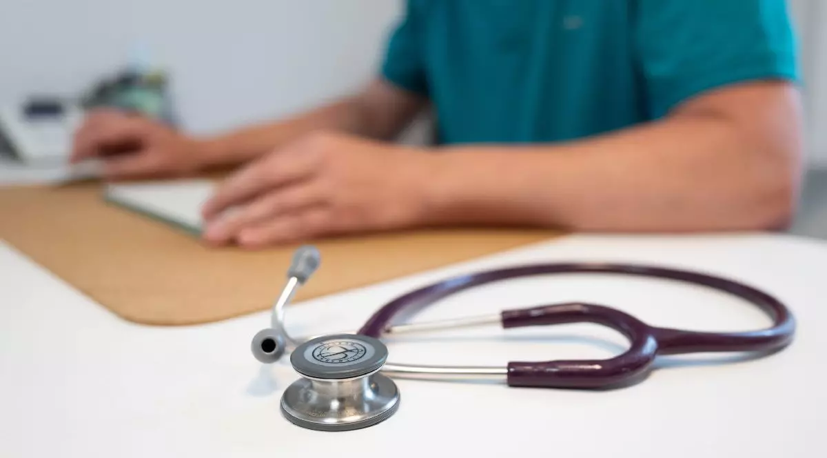 Un medic care are pe birou un stetoscop scrie ceva- concediu medical. Reula primei zile de concediu medical. Foto Hepta