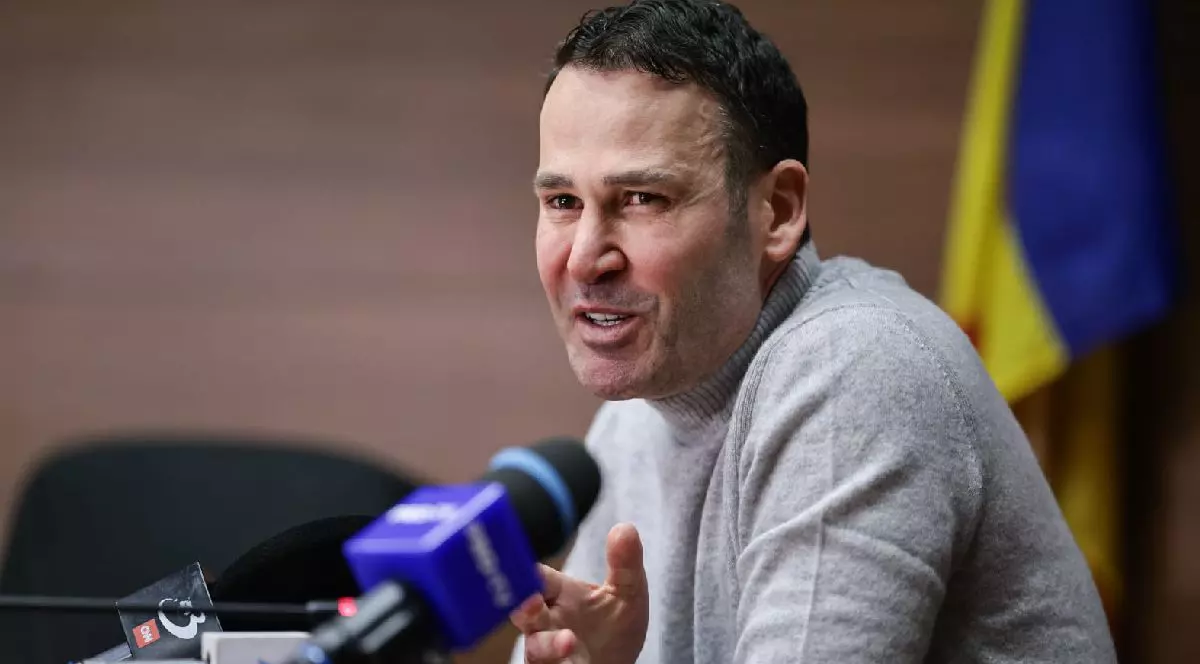 Robert Negoiță, cu părul scurt și negru, îmbrăcat cu un pulover gri deschis, vorbind la microfon în timpul unei conferințe de presă. În fundal se vede un steag.