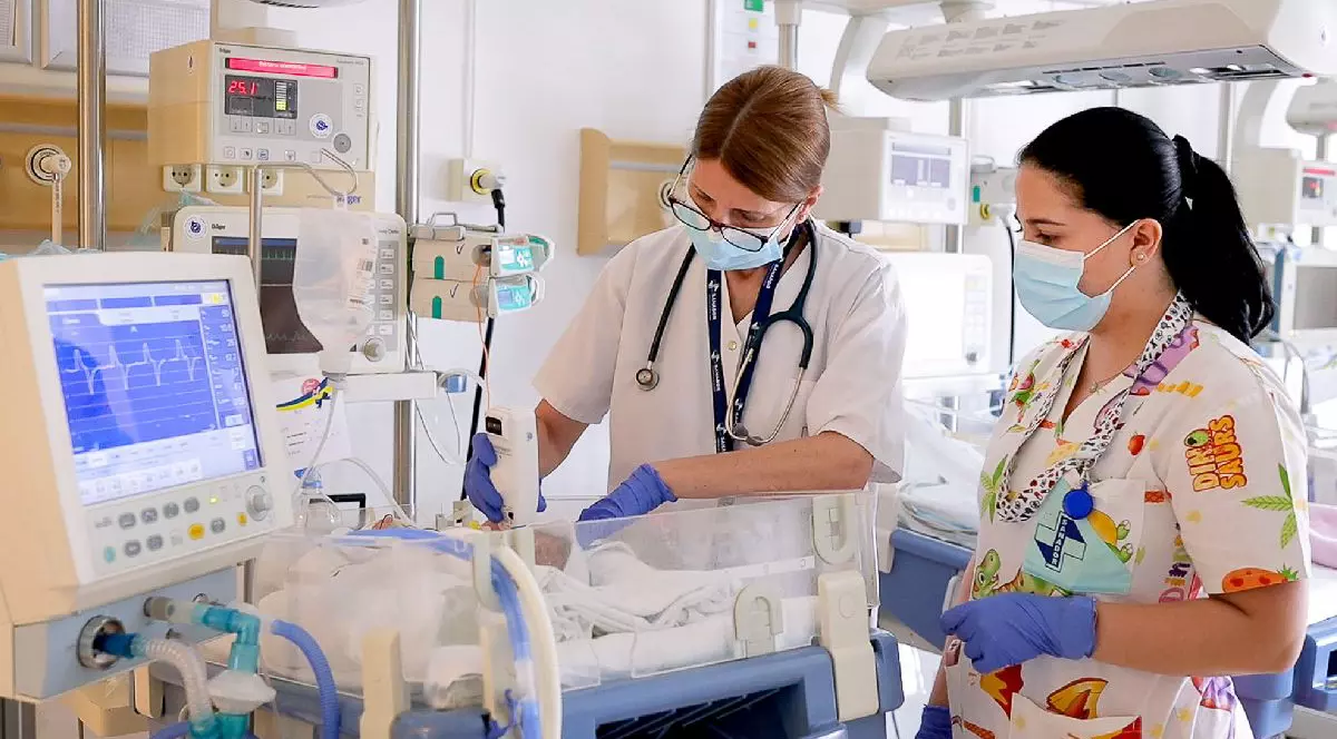 O doctoriță și o asistentă medicală consultă un bebeluș într-un salon de spital