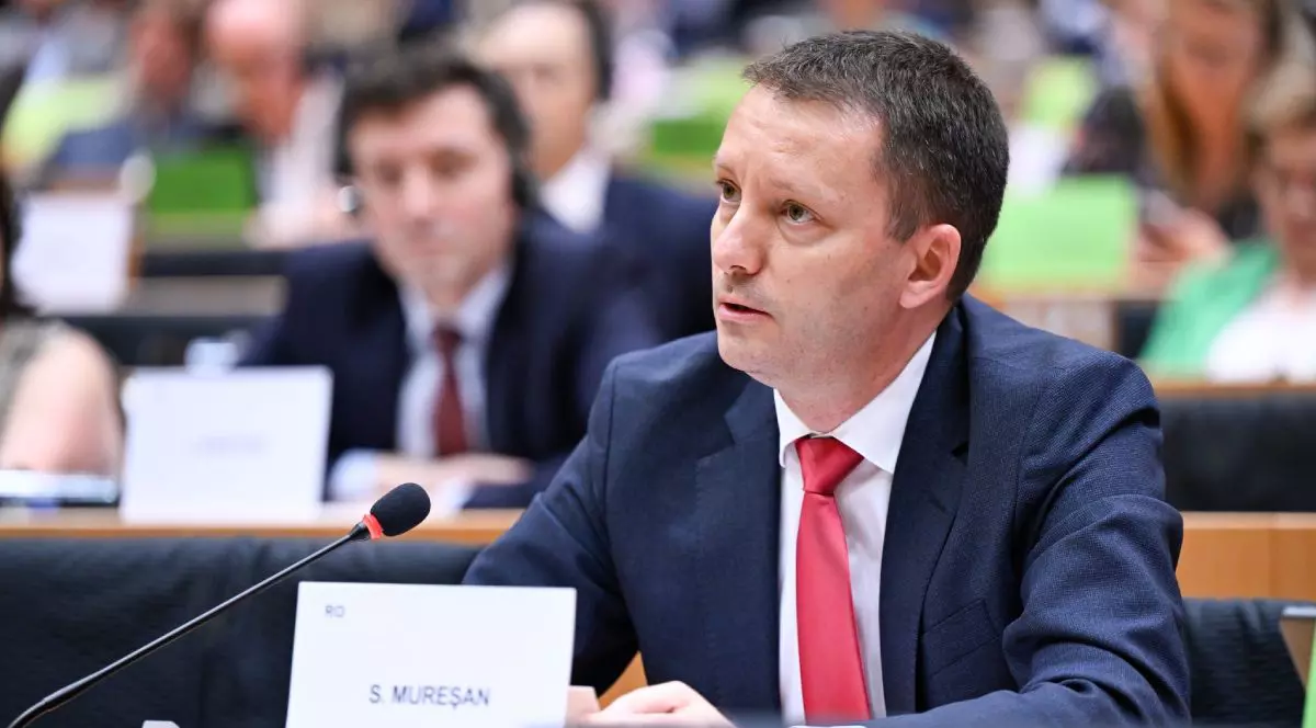 Siegfried Mureșan, îmbrăcat cu un costum albastru închis, cămașă albă și cravată roșie, la un pupitru în Parlamentul European
