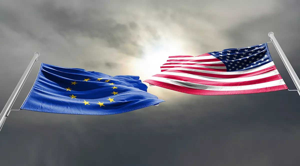 Steagul UE, albastru cu stelute galbene si steagul SUA, linii rosii si albe si stelute alte pe albastru, pe un fundal cu un soare acoperit de nori gri