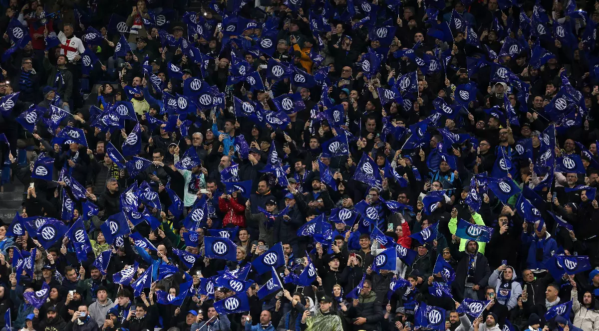 Tribunele stadionului sunt pline de suporteri ai Inter Milano, care flutură steaguri alb-albastre și creează o atmosferă spectaculoasă.