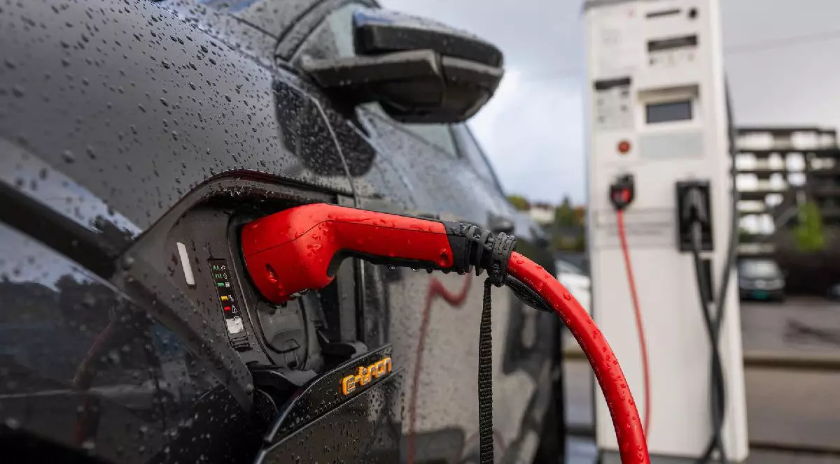 Fotografie cu o mașină neagră care e încărcată la o stație de încărcare electrică, cu un cablu de încărcare roșu conectat la portul vehiculului și picături de apă pe suprafața mașinii.