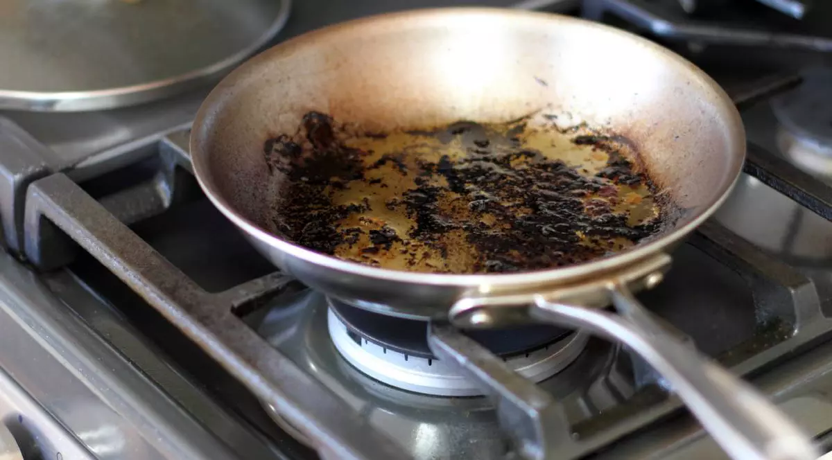 Cadru apropiat cu o tigaie folosita, murdara, arsă si cu grasime, pe ochiul unui aragaz