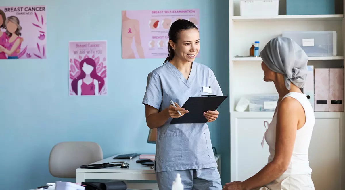 O femeie imbracata in echipament medical albastru aflata intr-un cabinet medical cu un clipboard in mana sta de vorba cu o tanara cu un batic pe cap. traseu bolnavi cancer in Romania. Harta serviciilor oncologice. Foto: Shutterstock