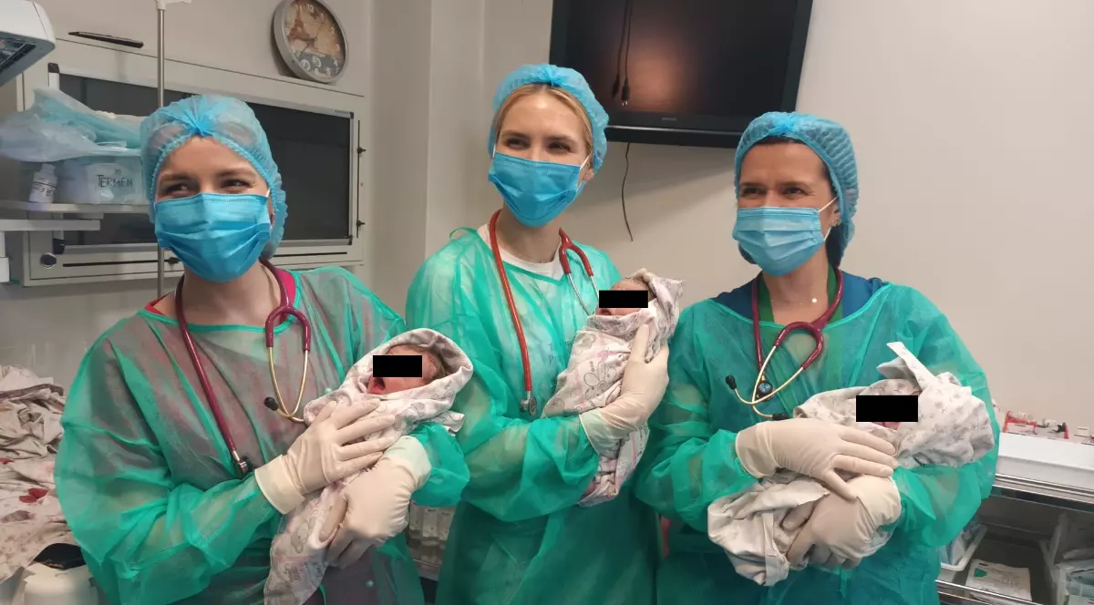 Trei femei, asistente medicale în combinezoane verzi, țin în mână trei bebeluși