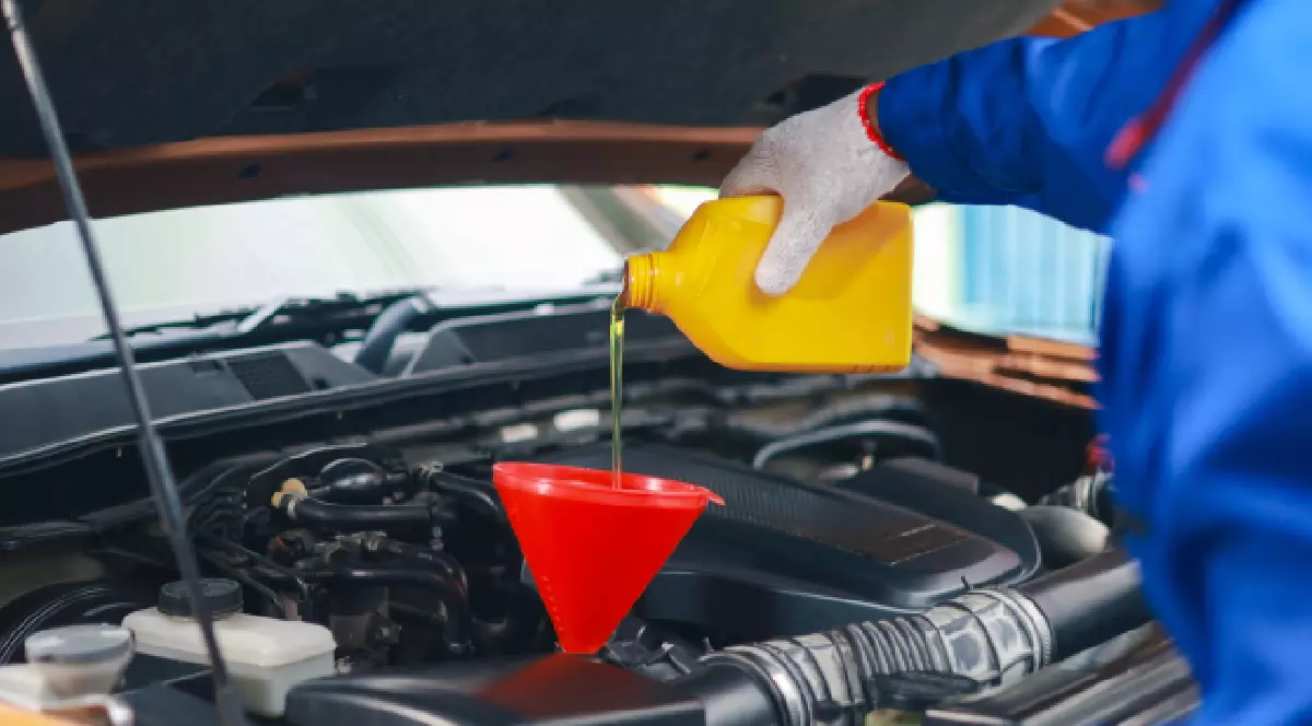 Un bărbat toarnă uleiul în motorul mașinii.
